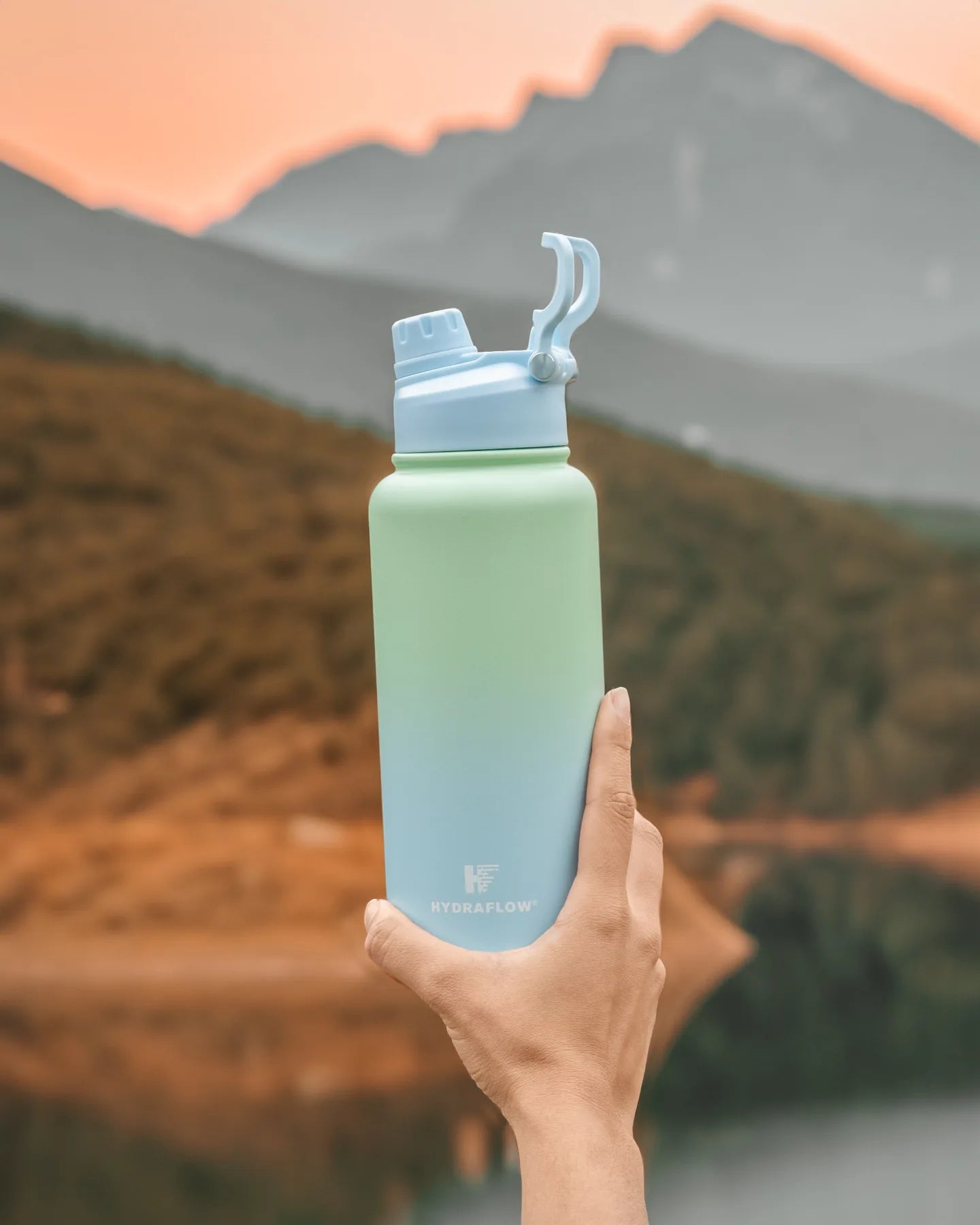 Mint and blue ombre Hydraflow bottle held against a mountain backdrop