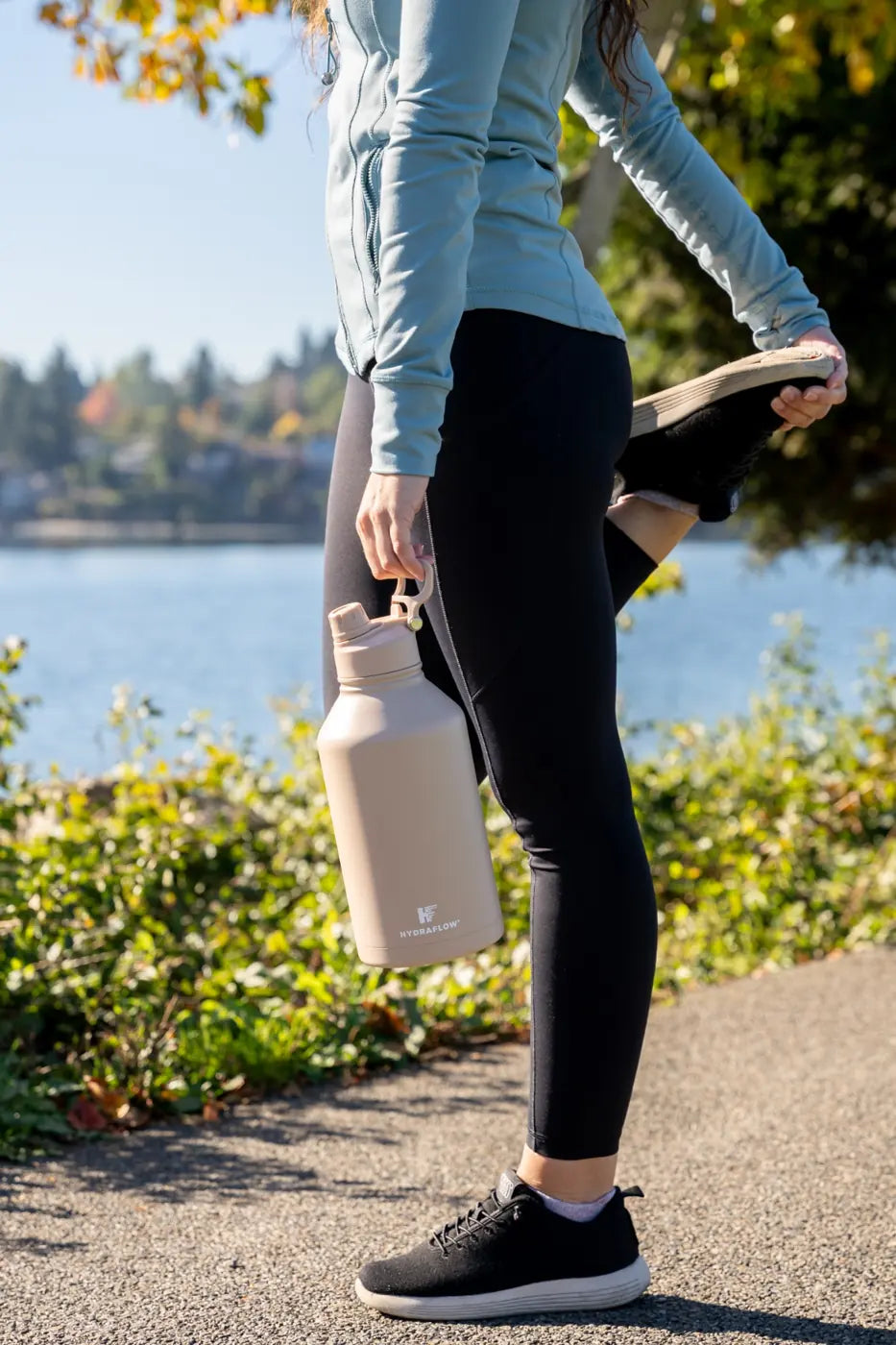 Woman carrying a cream Hydraflow bottle on a lakeside walk
