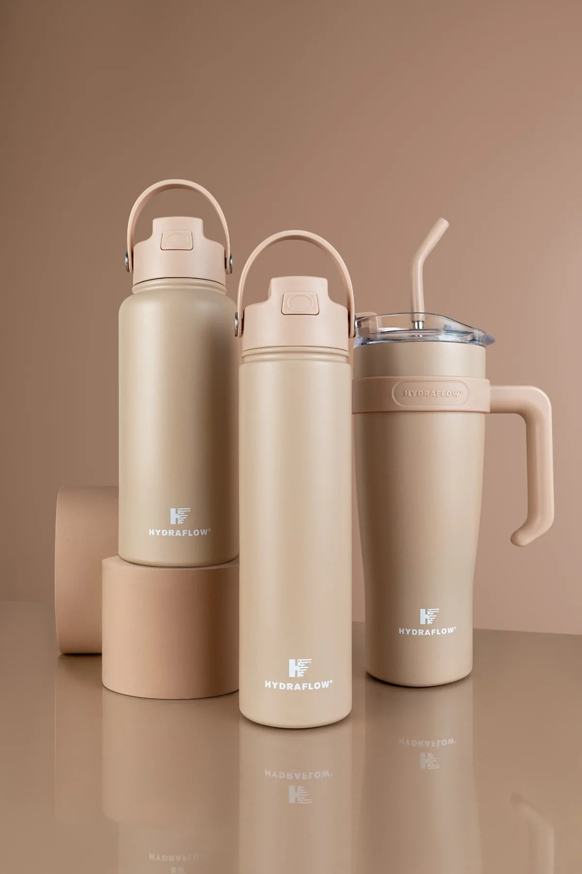 Three cream Hydraflow bottles and tumblers arranged on warm studio plinths